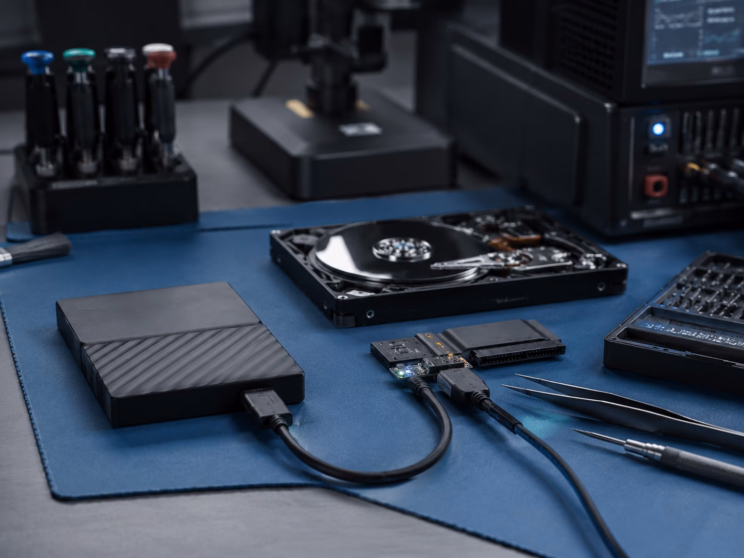 Externe Festplatte mit USB-Kabel, ge&ouml;ffnete Festplatte, Adapterelektronik und Pr&auml;zisionswerkzeuge auf einem technischen Laborarbeitsplatz f&uuml;r Datenrettung.
